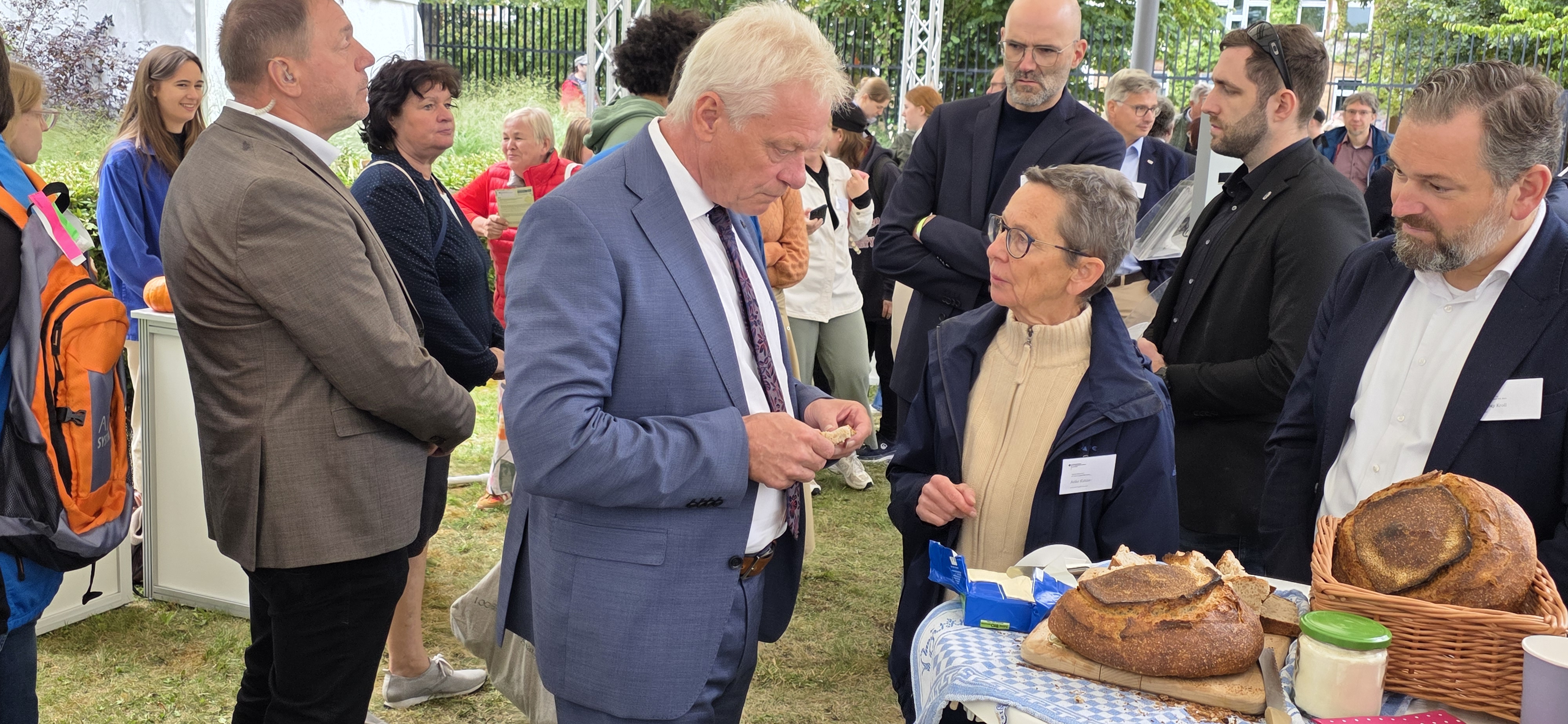 Content_Bild_1 Zwei Menschen in Menschenmenge im Gespräch, rechts Backwaren auf Stehtisch